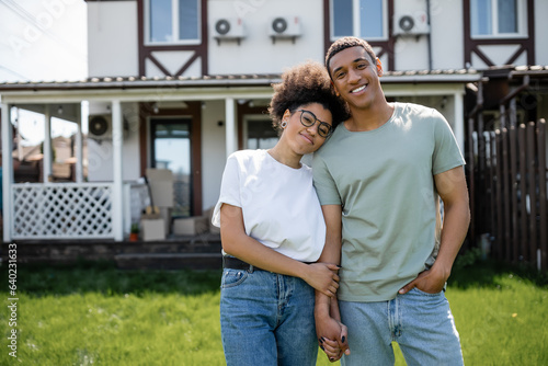 Schilderij op canvas happy african american couple holding hands and looking at camera near new house
