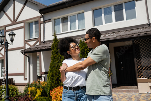 cheerful african american couple hugging while standing near new house outdoors