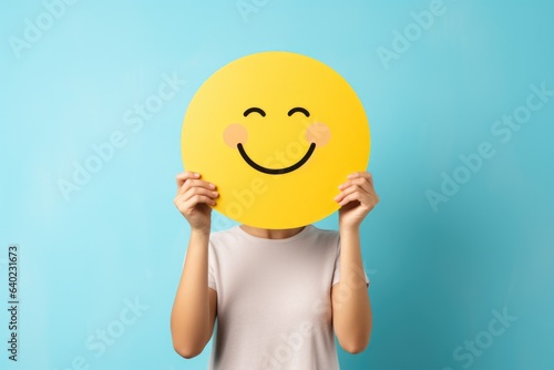 a woman holding up a yellow smiley face mask