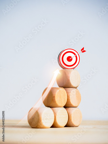 3d Target icon on top of wooden blocks with rise up arrows on bar graph chart steps on white background, vertical style, business growth process, profit, investment, economic improvement concepts. photo