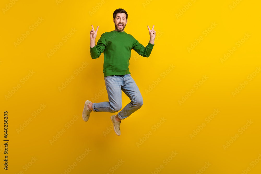 Obraz premium Full size body photo of jumping overjoyed crazy guy brunet businessman green pullover gesturing v sign isolated on yellow color background
