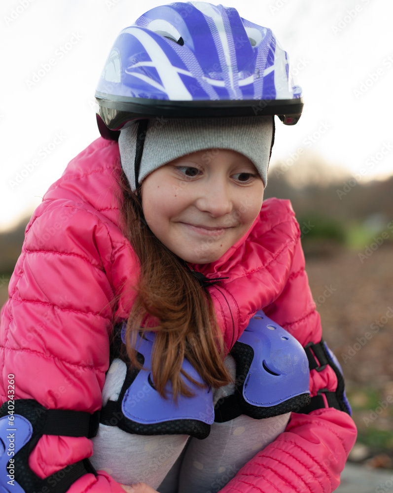 the girl is squatting and resting after roller skating. wearing a pink jacket and a purple helmet the girl is squatting and resting after roller skating. wearing a pink jacket and a purple helmet