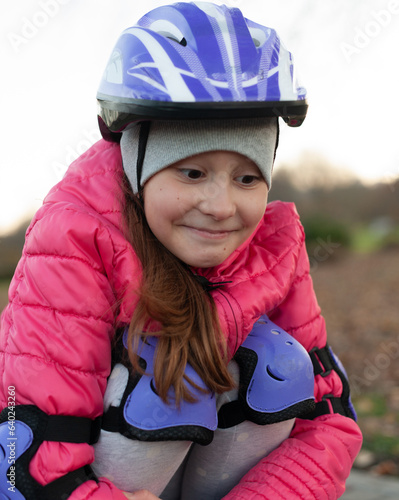 the girl is squatting and resting after roller skating. wearing a pink jacket and a purple helmet