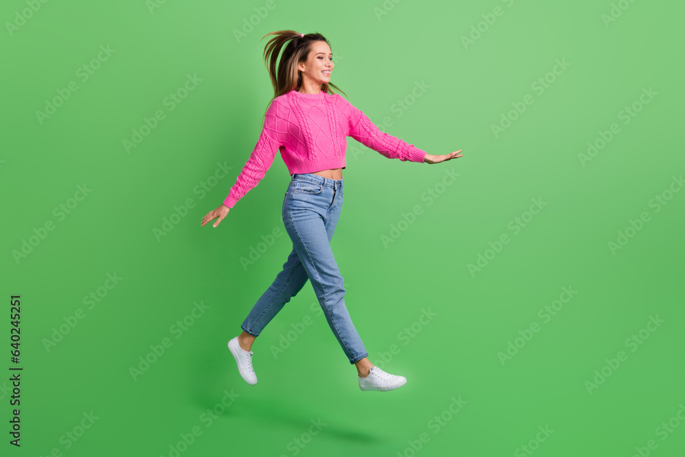 Full size photo of good mood satisfied girl wear pink pullover jeans go shopping look empty space isolated on green color background Full size photo of good mood satisfied girl wear pink pullover jeans go shopping look empty space isolated on green color background