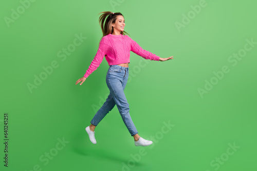 Full size photo of good mood satisfied girl wear pink pullover jeans go shopping look empty space isolated on green color background