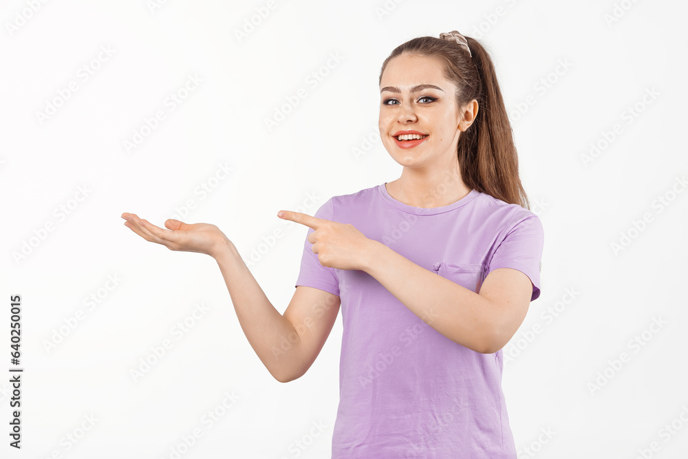 Smiling young woman with long hair points finger at banner, shows great promo offer aside, stands in casual t shirt over white background Smiling young woman with long hair points finger at banner, shows great promo offer aside, stands in casual t shirt over white background
