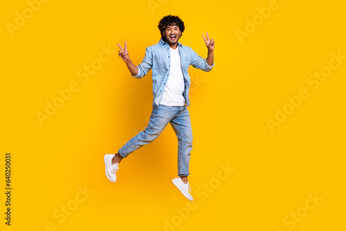 Full length photo of positive funny guy dressed denim jacket jumping high showing v-signs isolated yellow color background