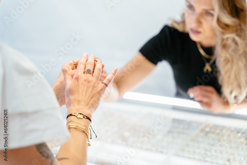 Close-up of woman's hand trying on a beautiful ring with a precious stone on her finger in a jewelry store. Business woman owner of jewelry boutique consulting female client.