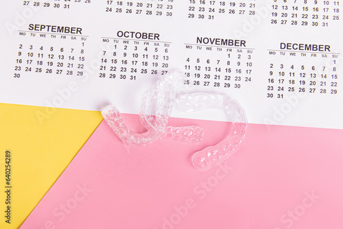 Aligners and calendar on pink and yellow background. Invisible aligners. Duration of treatment