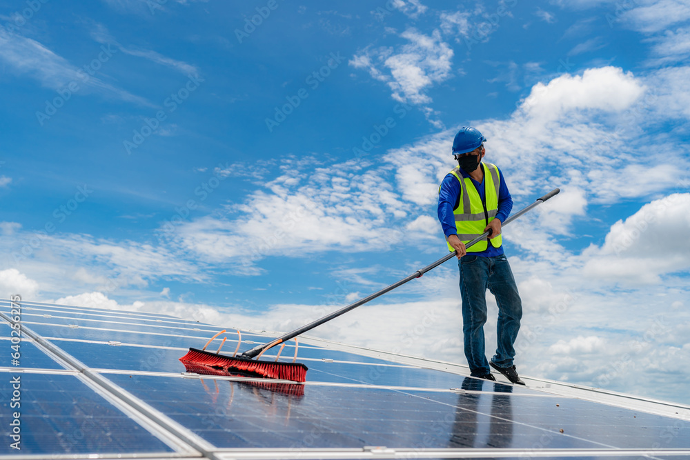 Professional worker cleaning solar panels with brush and washing with water on roof structure of building factory. Technician using mop to clean the dirty and dust, green electricity energy technology Professional worker cleaning solar panels with brush and washing with water on roof structure of building factory. Technician using mop to clean the dirty and dust, green electricity energy technology