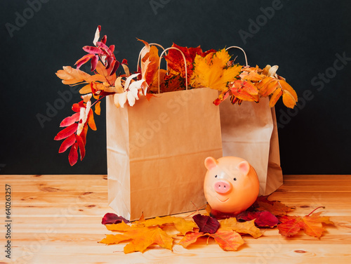 Colorful autumn leaves in paper bags and piggy bank near. Sale and shopping concept.