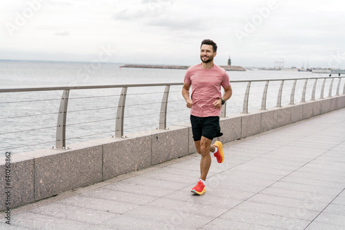A runner is a man in sportswear and running shoes, in full height. An athlete is a strong person who trains alone, uses a fitness watch and an application for sports. © muse studio