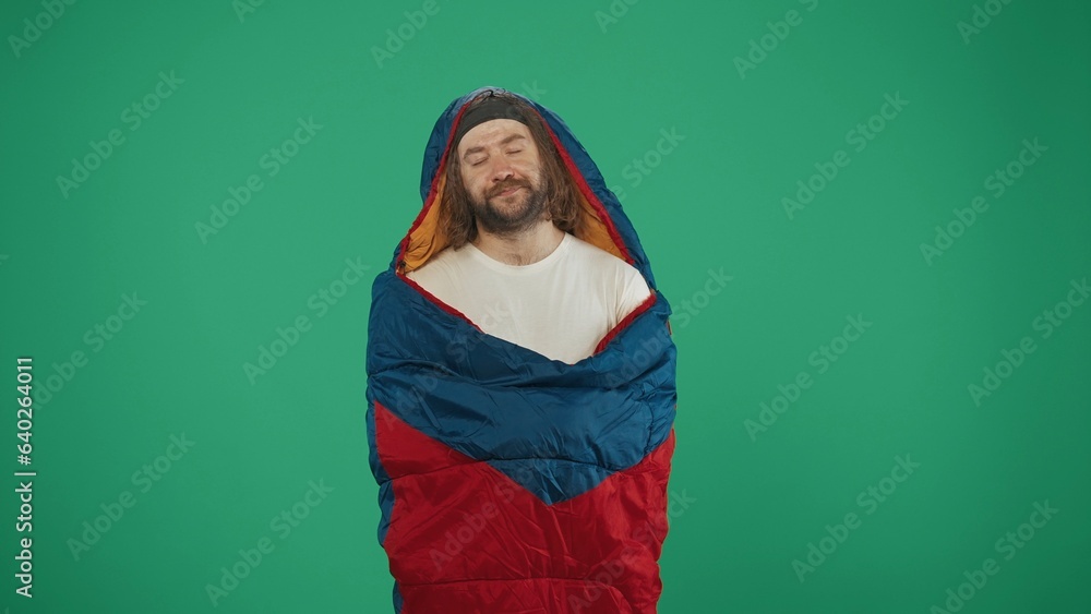 Man tourist inside a sleeping bag falling asleep. Isolated on green background. Man tourist inside a sleeping bag falling asleep. Isolated on green background.