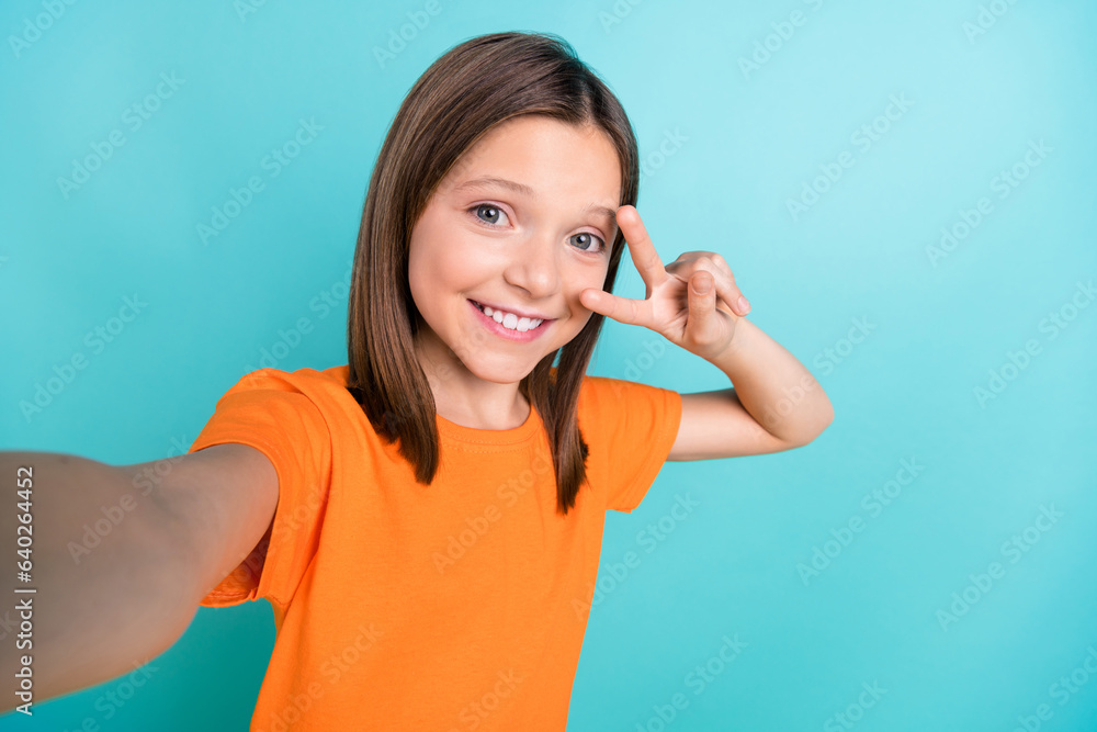 Photo of adorable cheerful little girl wear orange stylish t-shirt doing selfie show v-sign on eye isolated on teal color background Photo of adorable cheerful little girl wear orange stylish t-shirt doing selfie show v-sign on eye isolated on teal color background