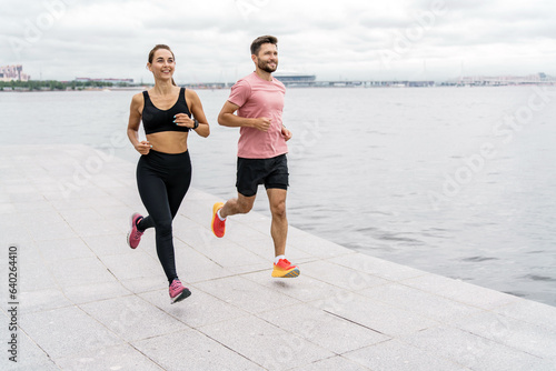 Using a fitness watch on your hand. Partners athletes people training together jogging. Runners are a man and a woman in sportswear and running shoes, in full height.