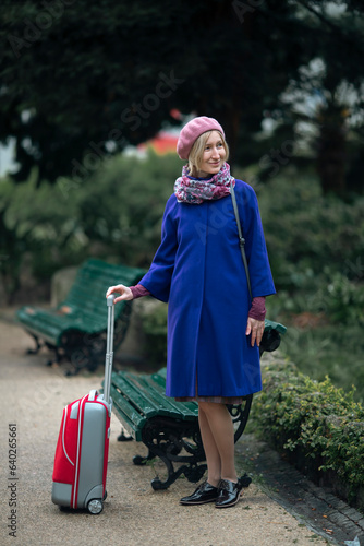 Obraz na płótnie There is a woman walking down the street with a red suitcase in her hand. w salonie