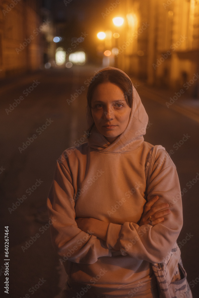 young thoughtful woman stands on road in beige hoodie. walk in evening in light of lanterns, portrait of female alone. freedom loneliness of modern generation. Travel and rest alone, mental health young thoughtful woman stands on road in beige hoodie. walk in evening in light of lanterns, portrait of female alone. freedom loneliness of modern generation. Travel and rest alone, mental health