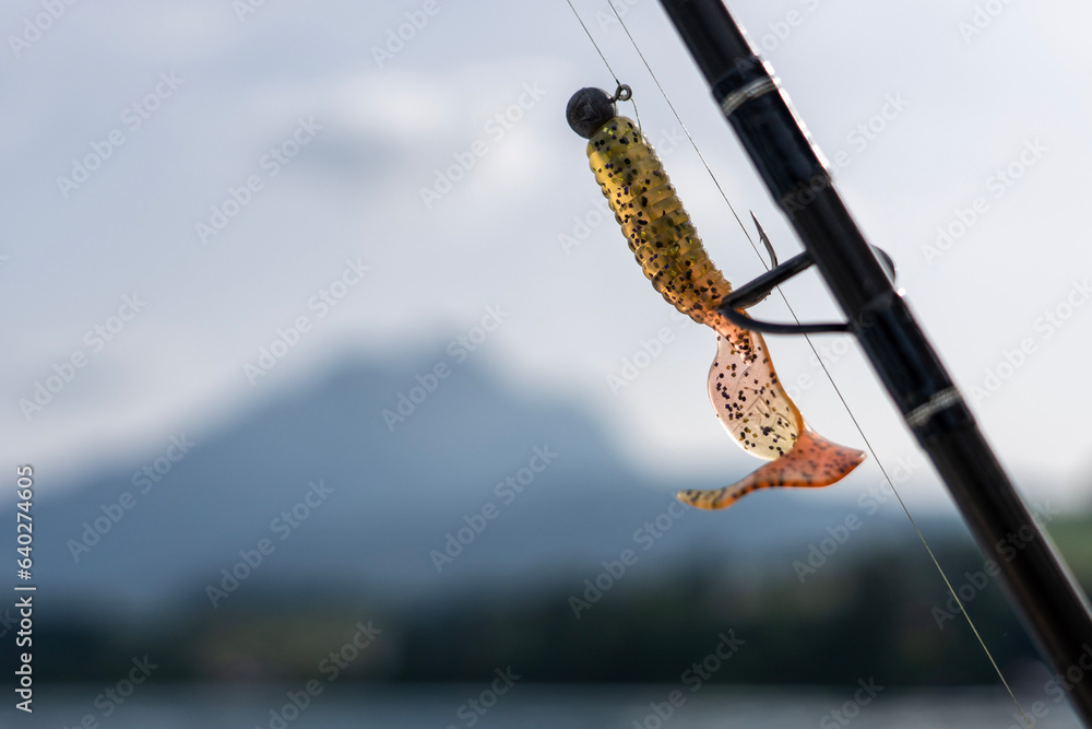 Semi-Transparent fishing lure hooked on a rod with the sunlight shining through and the pilatus mountain blurry in the background 