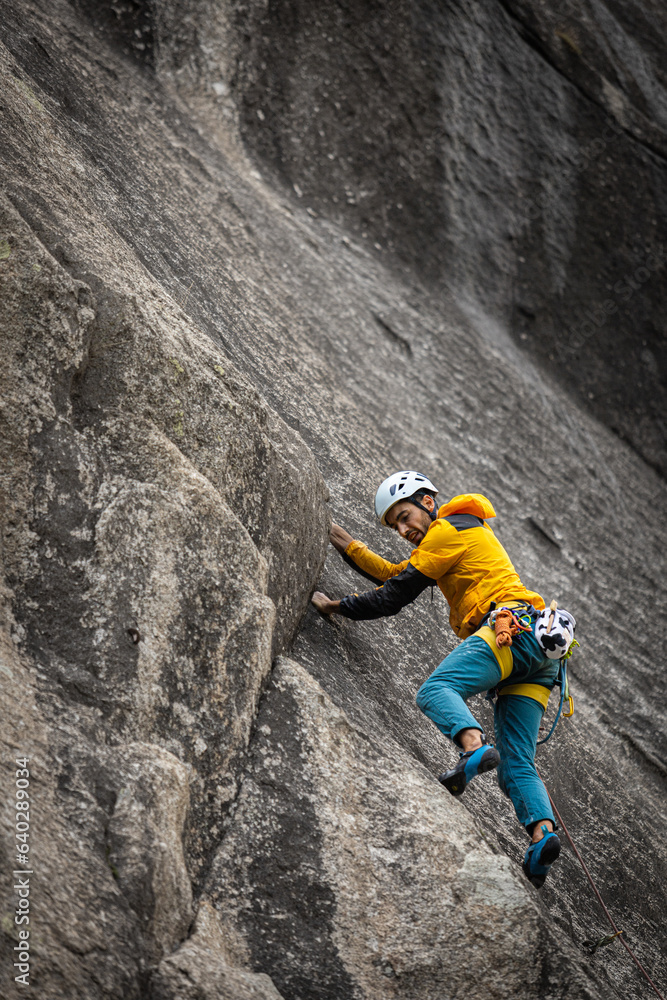 Person climbing in high mountains with yellow jacket rope and helmet in nature, confidence and risk, safety