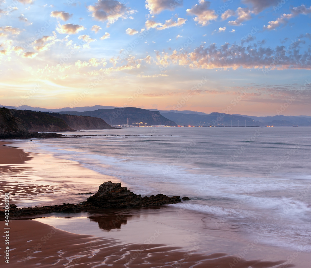 Twilight ocean rocky coast landscape with sky reflection on wet sand of beach (Spain).
