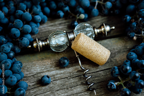 Corkscrew with corck among ripe grapes lay on a rustic wood table. Concept of autumn, vineyards, winemaking photo