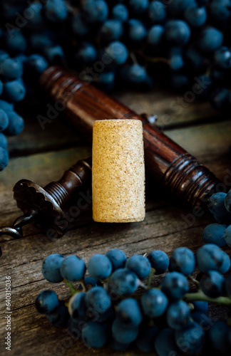 Vintage corkscrew with corck among ripe grapes lay on a rustic wood table. Concept of autumn, vineyards, winemaking