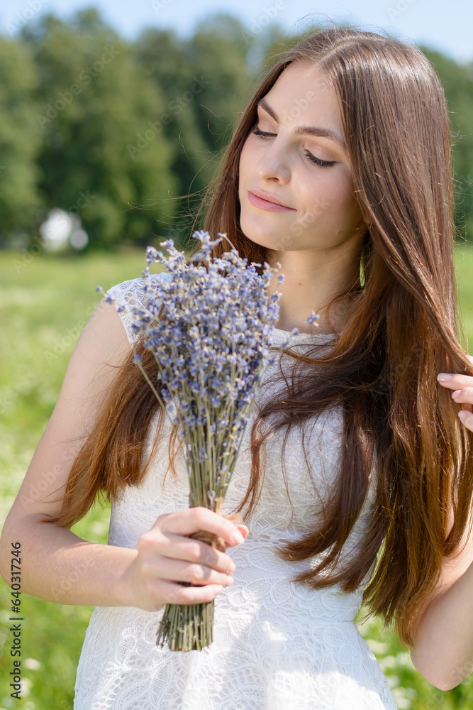 Beautiful young woman with a bouquet of lavender at a flowery meadow in a white dress