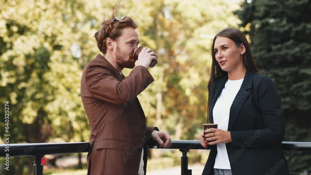 Two business partners, a bearded man, a brunette woman in formal suits, standing on the glass terrace of an office building in the city center, discussing a project and making a deal, holding a laptop Two business partners, a bearded man, a brunette woman in formal suits, standing on the glass terrace of an office building in the city center, discussing a project and making a deal, holding a laptop