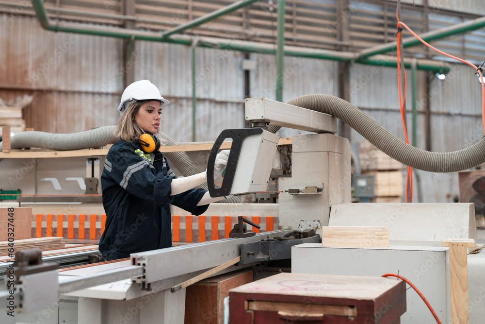 Woman worker operating CNC machine for cutting wood in factory. Female technical in uniform with helmet safety working produce wooden pallet at manufacturing plant. Woman worker operating CNC machine for cutting wood in factory. Female technical in uniform with helmet safety working produce wooden pallet at manufacturing plant.