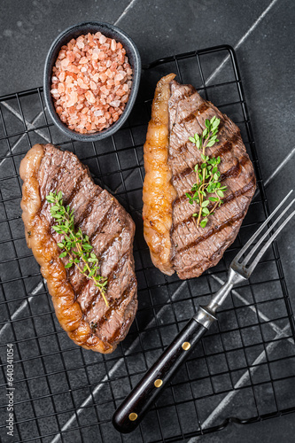 Grilled top sirloin or cup rump beef meat steak on a rack. Black background. Top view