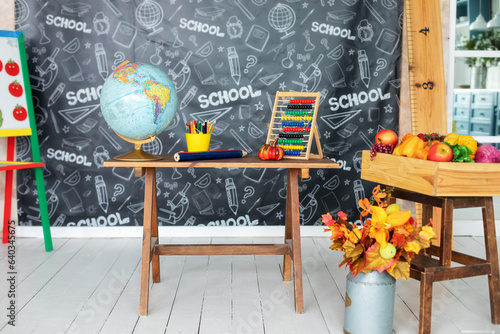 Back to school. Interior of elementary school. Empty classroom with blackboard and wooden table. Kindergarten. Globe, pencils and stationery on table against the background of a chalkboard.	
