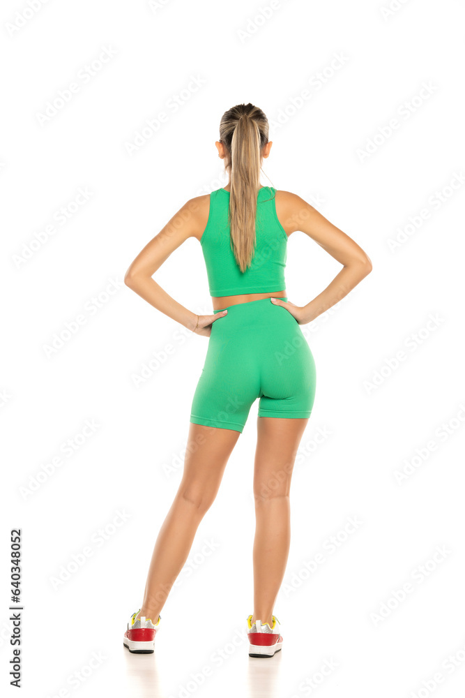 young sporty woman in green shorts and top posing on white background. Back view young sporty woman in green shorts and top posing on white background. Back view