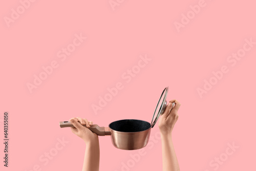 Female hands holding cooking pot with opened lid on pink background