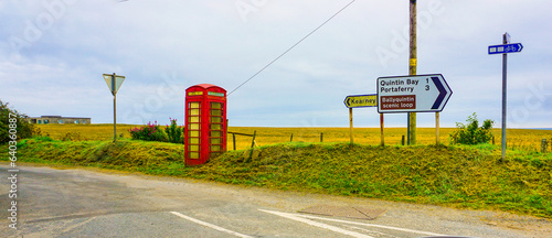 Along The Mourne Coastal Route, in County Down, Northern Ireland, an old disused red telephone box near road signs for Kearney and Portaferry. photo