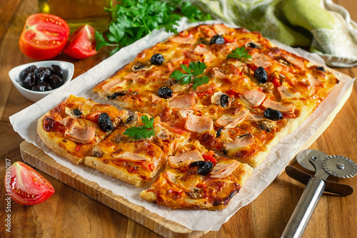 Fresh homemade rectangular pizza with ham, tomatoes and olives