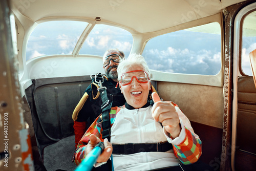 Scared senior woman getting ready to skydive out of an airplane with her skydiving instructor photo