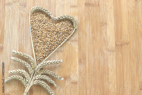 wholewheat heart shape with wheat ears whole grain healthy food for heart disease concept with copy space. Wholewheat flour, wheat ears wheat on the bamboo wood board background. Top view.  photo