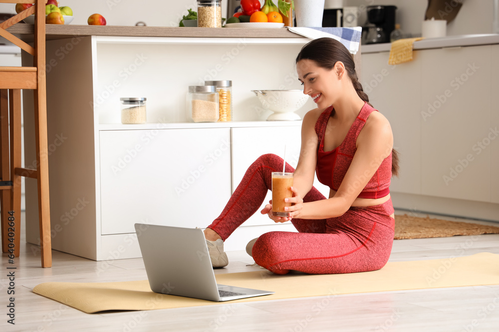 Sporty young woman with healthy smoothie and laptop in kitchen Sporty young woman with healthy smoothie and laptop in kitchen