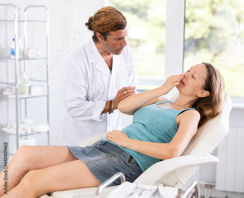 Adult male doctor in medical uniform examining face of woman patient in medical room..