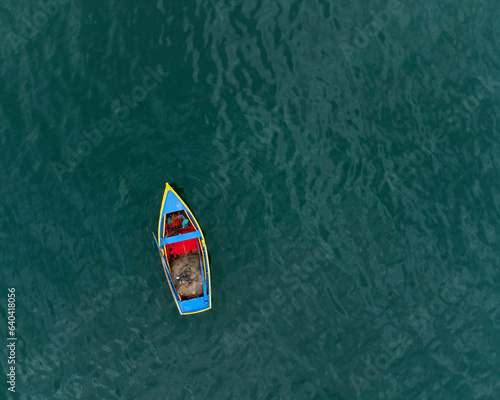 image from above of a yellow, blue and red fishing boat in a quiet blue green sea © Gambohan