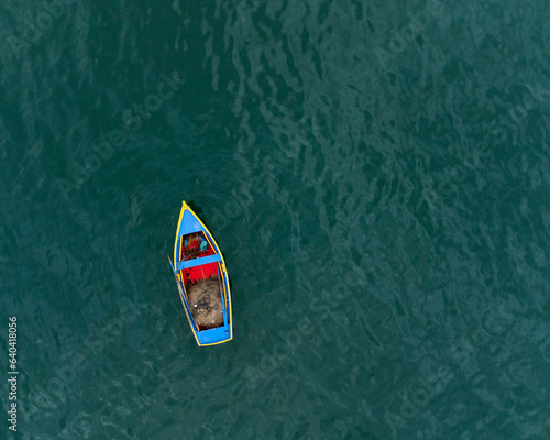 image from above of a yellow, blue and red fishing boat in a quiet blue green sea