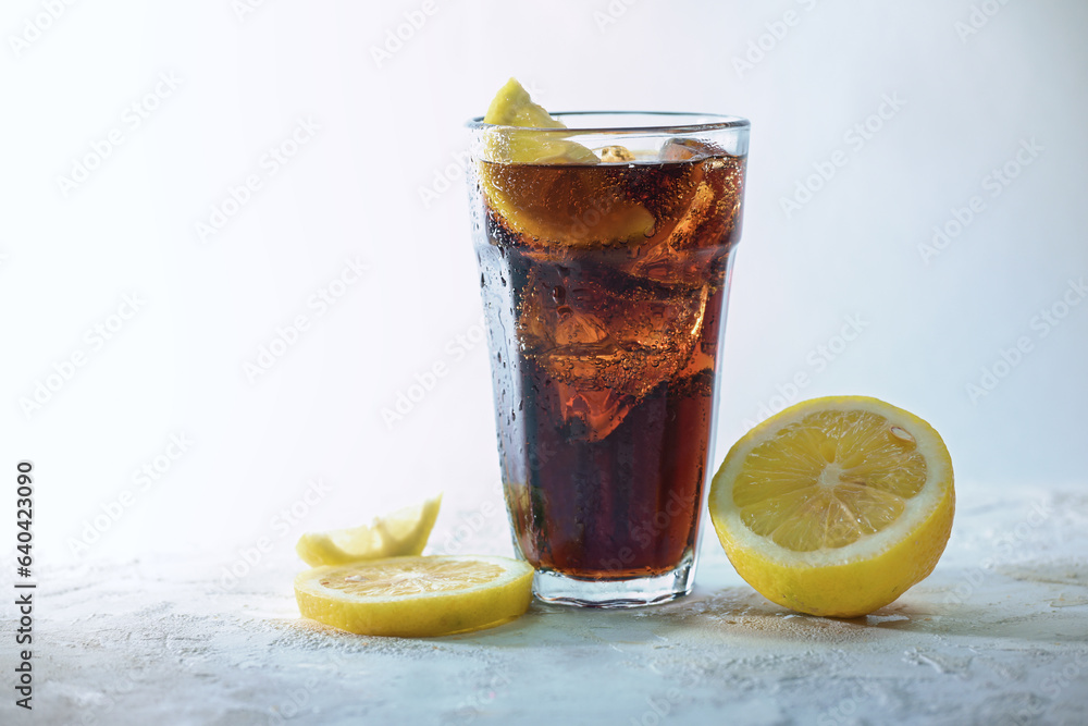 Fresh cola with ice cubes and lemon slices in a drinking glass against a light blue gray background, refreshing sweet caffeine drink, copy space, selected focus Fresh cola with ice cubes and lemon slices in a drinking glass against a light blue gray background, refreshing sweet caffeine drink, copy space, selected focus