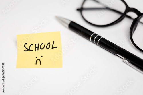 a yellow piece of paper with the inscription "SCHOOL" on a white background, glasses and a pen next to it (selective focus"
