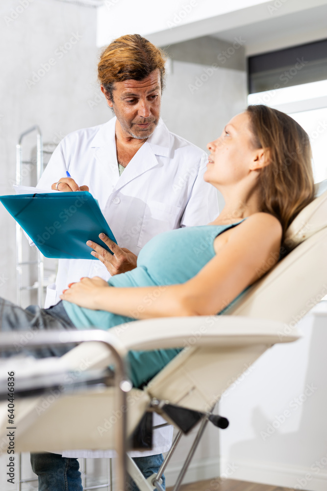 Obraz premium Friendly doctor holding document folder interacting attentively with adult woman lying on couch in clinic, gathering vital medical information and assessing patient health status