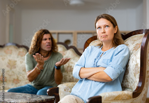 Upset casual couple speaking in raised tones with each other while sitting on the sofa in the living room