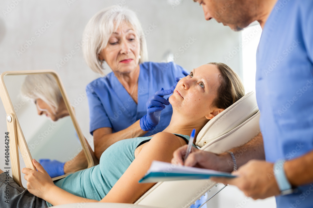 Plastic surgeon preparing patient for botulinum toxin injection treatment on face, while client observing herself in mirror.