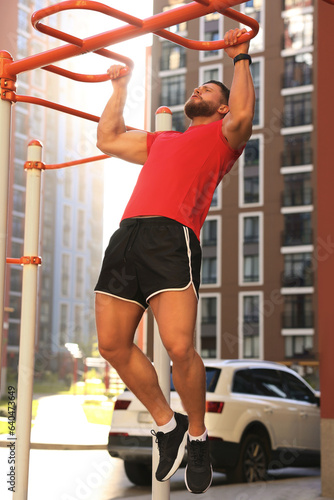 Man training on horizontal bars at outdoor gym on sunny day