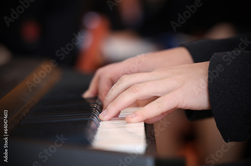 Close up of hands and fingers playing a keyboard or piano white keys. Audience blurred in background. Left hand in focus