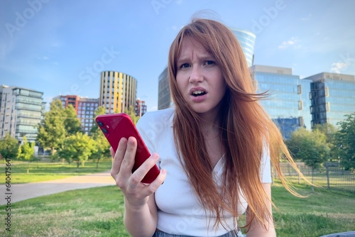 portrait of a young negative sad frustrated woman on the background of the business center in summer weather with cell mobile phone in hand