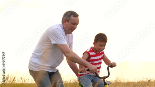 Happy father supports son training to ride bicycle at countryside lit by sunset © SUPER FOX